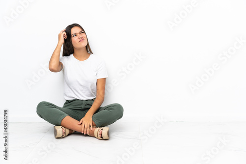 Teenager girl sitting on the floor having doubts and with confuse face expression