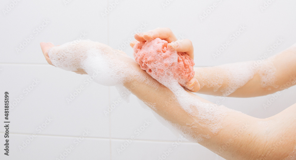 Fototapeta premium A girl in a white bathroom in foam rubs her hands with a pink washcloth