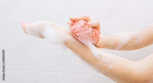 A girl in a white bathroom in foam rubs her hands with a pink washcloth