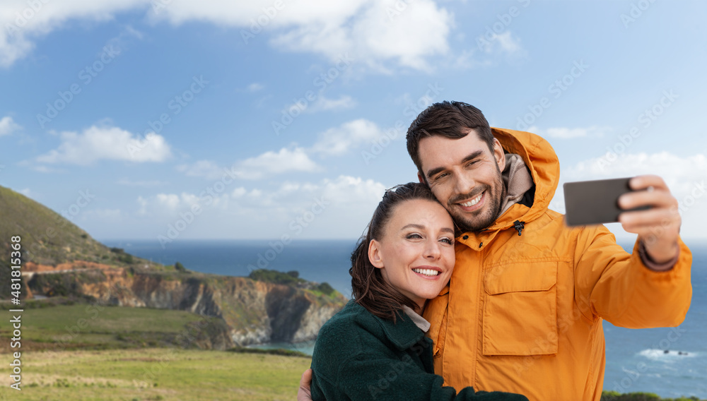 technology, travel and tourism concept - happy couple with smartphone over big sur coast in california background