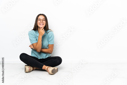 Teenager girl sitting on the floor with glasses and smiling