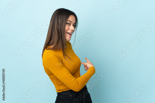 Teenager girl isolated on blue background pointing back