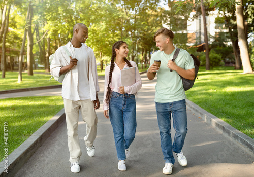 Three multiracial high-school students walking after study and talking in university campus outdoors