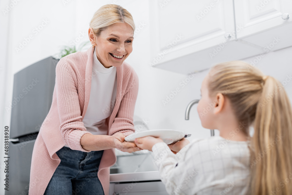 blurred girl holding plate while helping happy granny in kitchen. blurred girl holding plate while helping happy granny in kitchen.