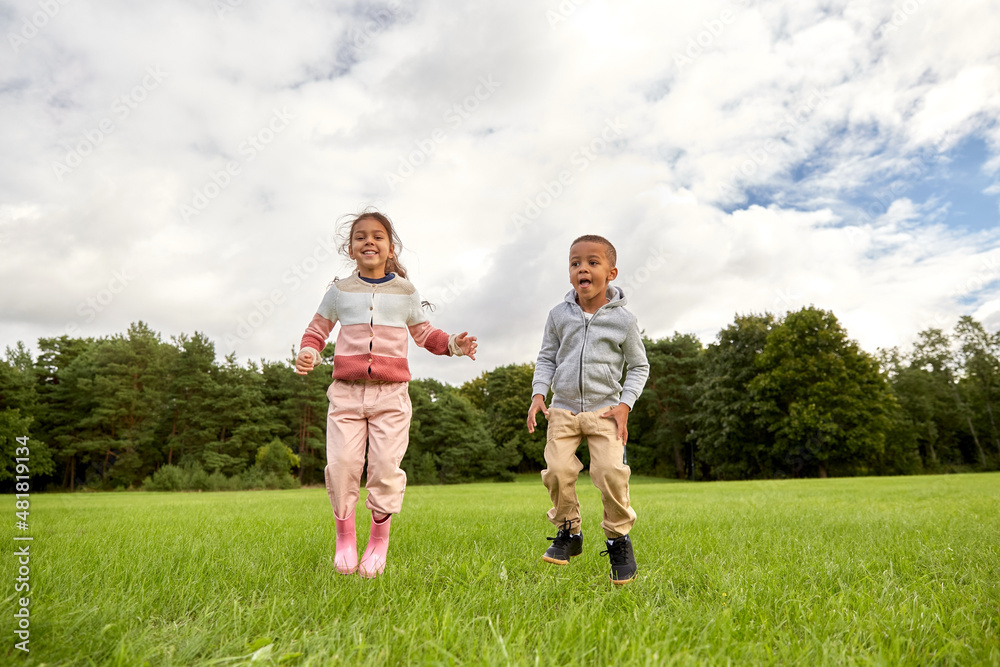 childhood, leisure and people concept - happy little boy and girl playing and jumping at park childhood, leisure and people concept - happy little boy and girl playing and jumping at park