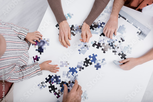 top view of cropped family playing jigsaw puzzle game on table.