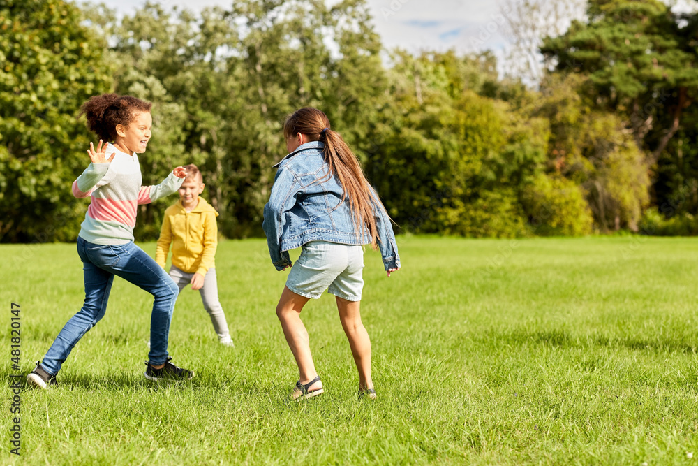 childhood, leisure and people concept - group of happy kids playing tag game and running at park