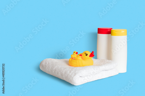 Obraz na płótnie Yellow rubber duck on soft white towel and two plastic white bottles with yellow and red caps on light blue background. Child bath accessories, baby care. Copy space. w salonie