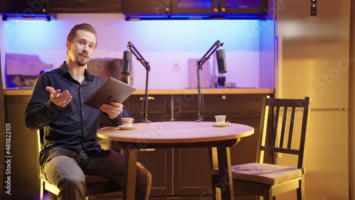 Male host with tablet on live podcast introduce empty seat guest round table discussion