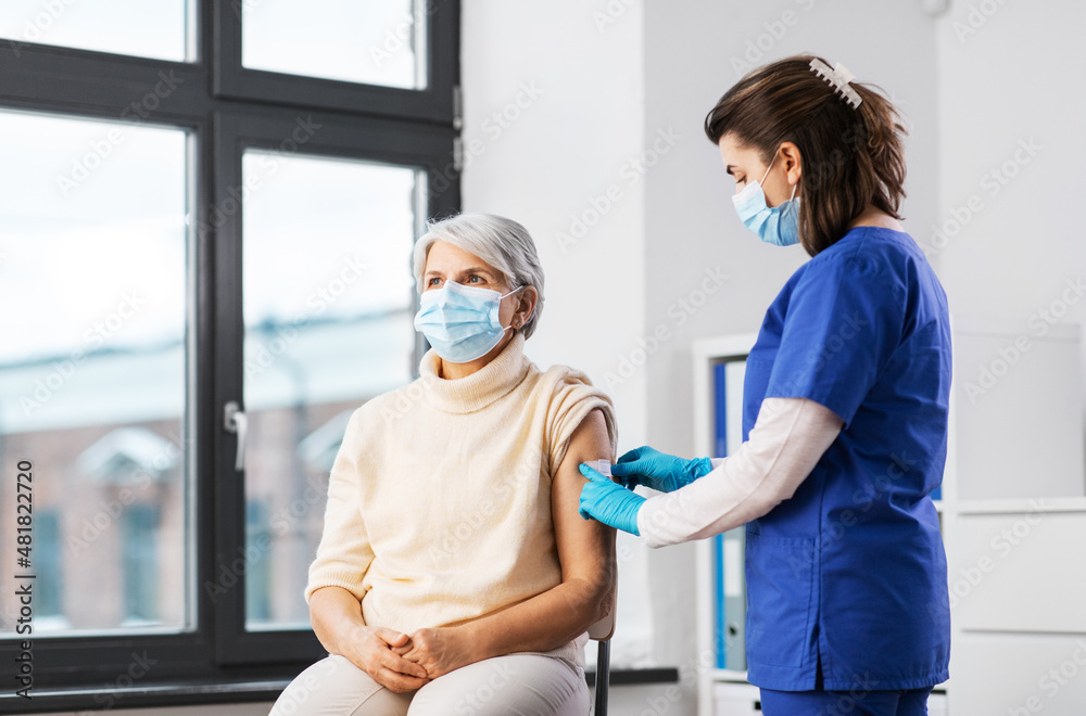 Obraz premium medicine, health and vaccination concept - doctor or nurse applying medical patch to vaccinated senior woman in mask at hospital
