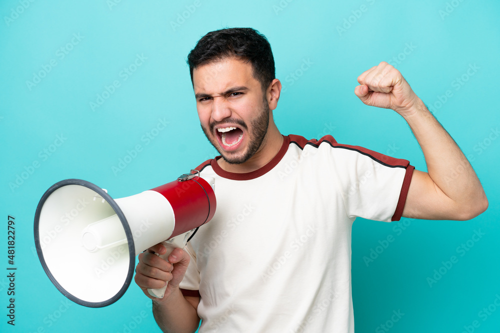 Young Brazilian man isolated on blue background shouting through a megaphone to announce something Young Brazilian man isolated on blue background shouting through a megaphone to announce something