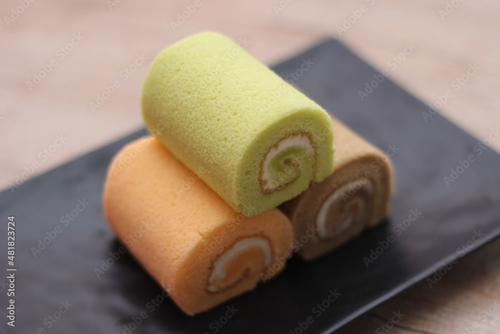 Fototapeta premium 3 Swiss rolls served in a black plate placed on a wooden table.
