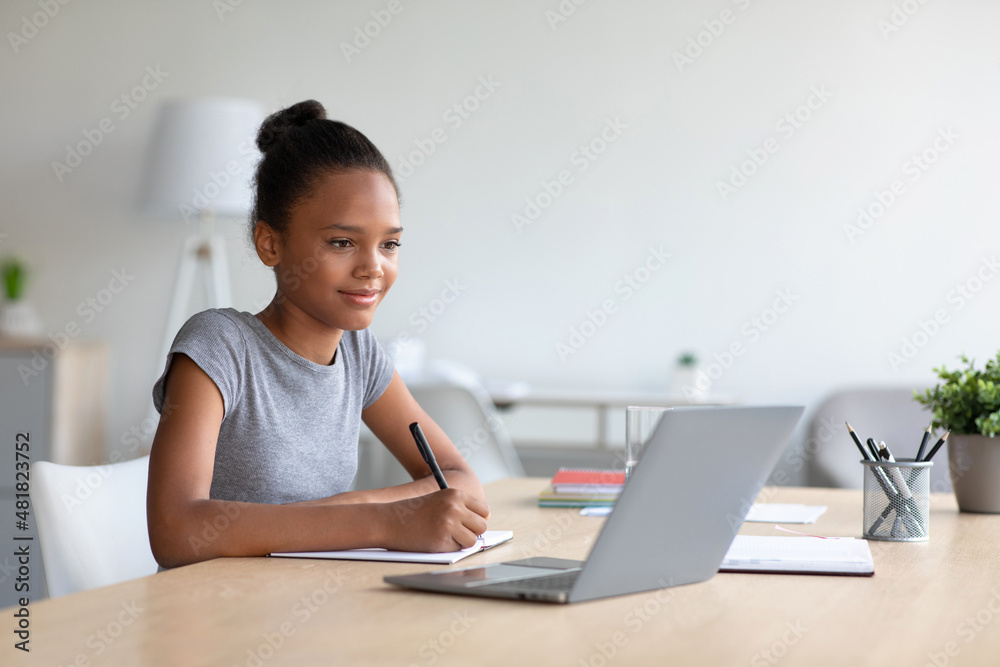 Smiling pretty smart teen african american girl student studying at home, watching online lesson on laptop Smiling pretty smart teen african american girl student studying at home, watching online lesson on laptop