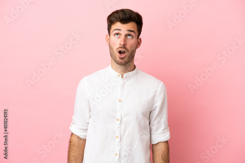 Young caucasian handsome man isolated on pink background looking up and with surprised expression