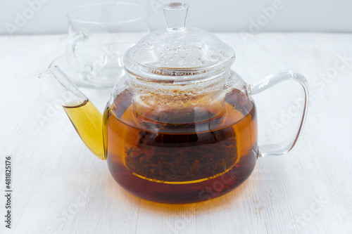 Black tea brewed in a glass teapot on a wooden white table.