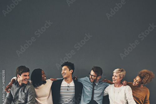 We make a great team. Studio shot of a diverse group of creative employees embracing each other against a grey background. photo