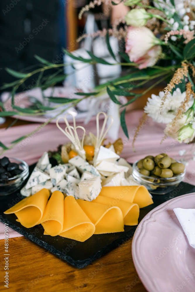 Cheese plate. Different types of cheese and olives on a black plate on a wooden table. 
An assortment of different types of cheese. 