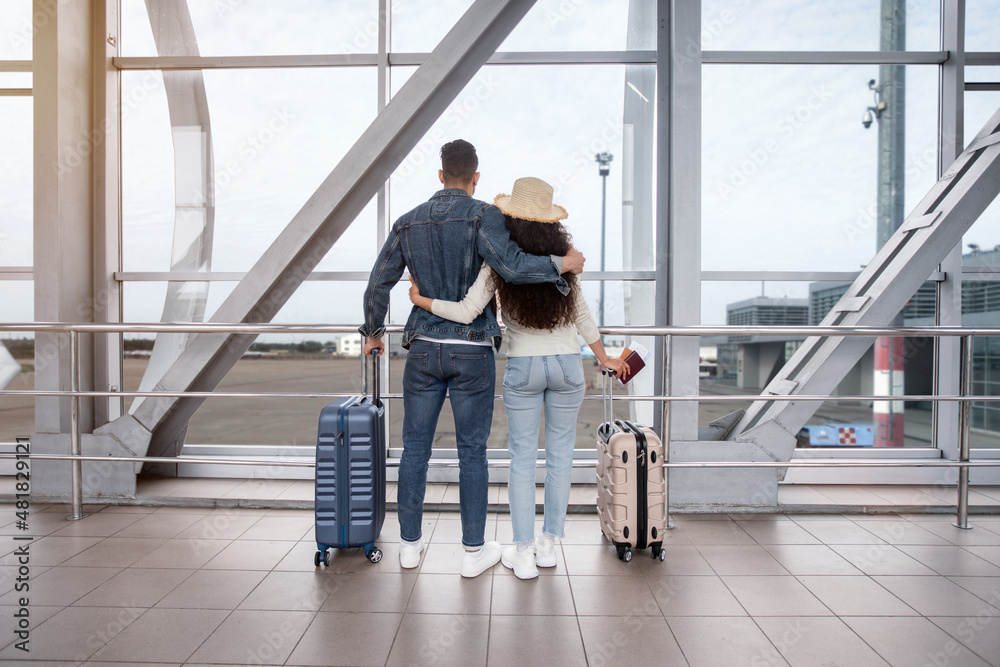 Rear View Of Romantic Couple Looking Out Of Window At Airport Terminal