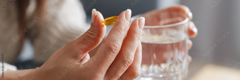 The close-up shot of a pill in a woman's hand with a glass of water