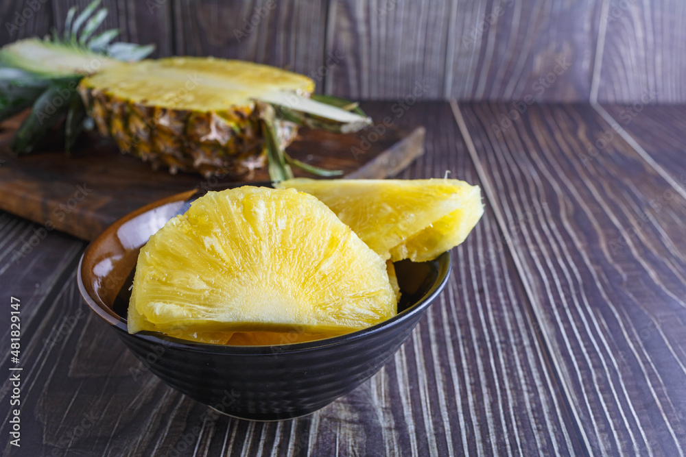 Fresh pineapple halved with pineapple slices in bowl on wooden table Fresh pineapple halved with pineapple slices in bowl on wooden table