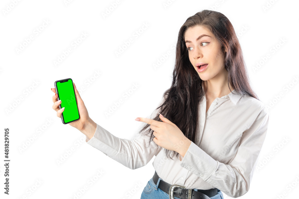 Amazed woman holding a smartphone (with green chroma key screen) looking it and pointing it with her finger. Isolated on white background. 20-22 years old. White european woman. Amazed woman holding a smartphone (with green chroma key screen) looking it and pointing it with her finger. Isolated on white background. 20-22 years old. White european woman.