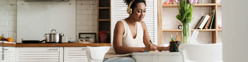 Black woman in headphones working with laptop while sitting at table Black woman in headphones working with laptop while sitting at table