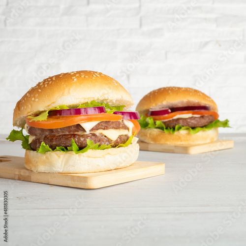 Hamburger and double burger with meat, salad, cheese, tomato and onion on wooden top and with white breakmates photo