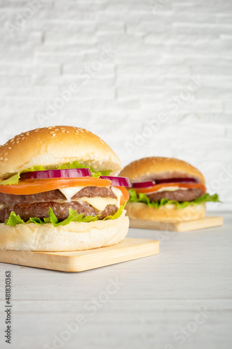 Hamburger and double burger with meat, salad, cheese, tomato and onion on wooden top and with white breakmates