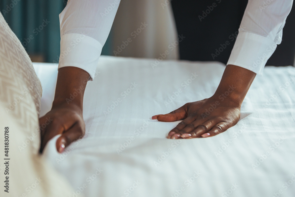 Housekeeper cleaning a hotel room. African housekeeper in a hotel room. Maid making bed in hotel room. Staff Maid Making Bed.  African housekeeper making bed.