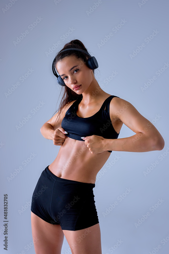 boxing sportswoman in headphones showing press cubes without fat on body in black top tracksuit, caucasian brunette lady is engaged in sport, after workout. sport, bodybuilding concept. isolated boxing sportswoman in headphones showing press cubes without fat on body in black top tracksuit, caucasian brunette lady is engaged in sport, after workout. sport, bodybuilding concept. isolated