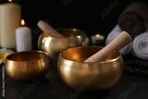 Golden singing bowls with mallets on black table against dark background