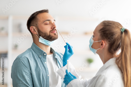 Female doctor making nasal coronavirus PCR test for millennial guy at clinic. Infectious disease protection concept photo
