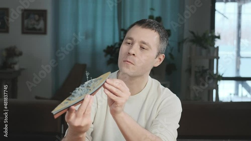 Adult cheerful man enthusiastically collects a plastic model of a historic ship.