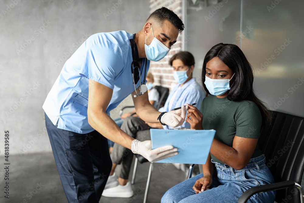 Black lady in face mask signing medical file before vaccination Black lady in face mask signing medical file before vaccination