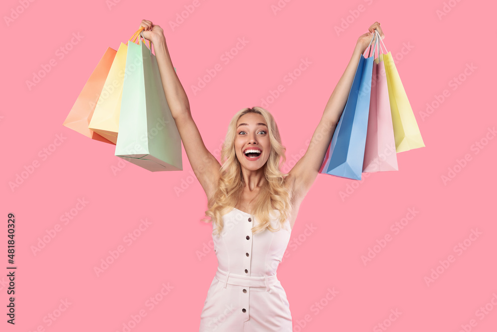 Excited blonde woman holding shopping bags at studio