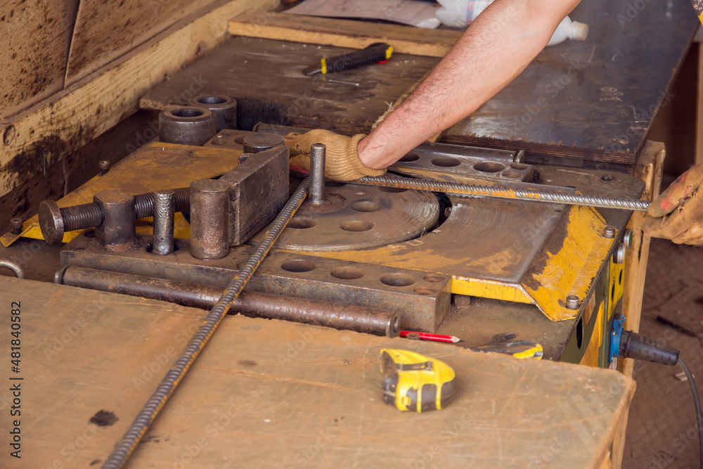 Assembly of reinforcing bars for pouring concrete. The worker is bending rebars with rebar bending machine in the site.