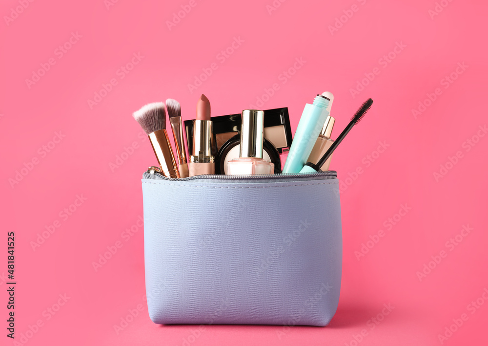 Cosmetic bag with makeup products and accessories on pink background
