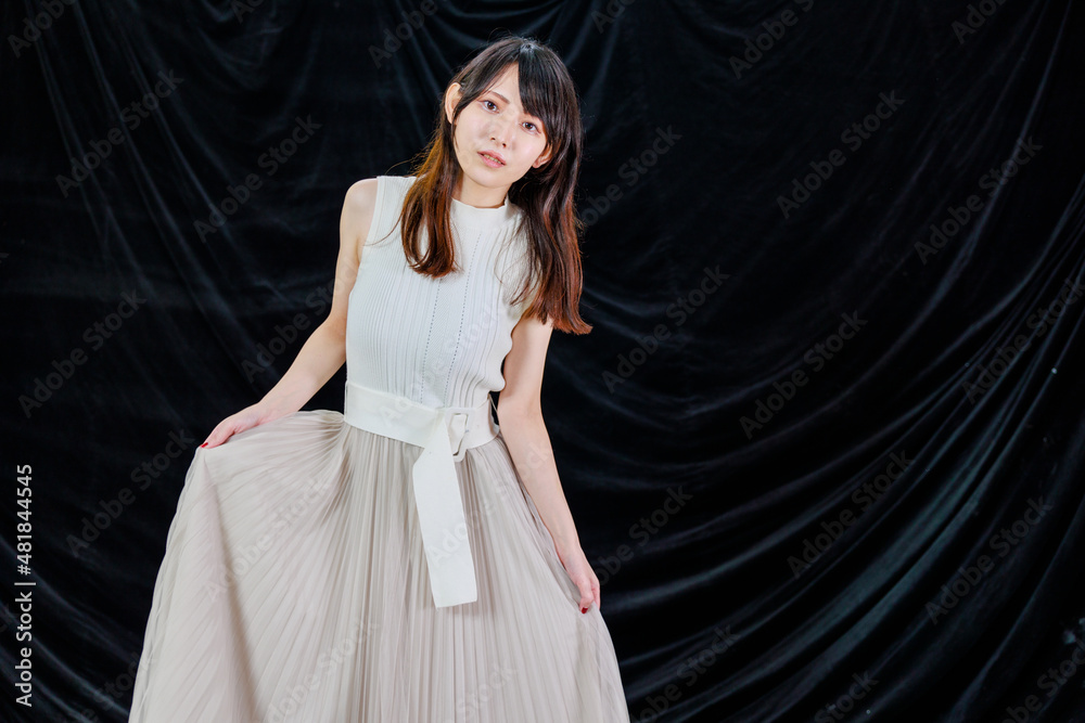 黒背景の前で微笑むロングスカートをはいた日本人女性の全身ポートレート