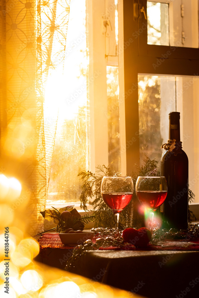 A bottle and two glasses of red wine in the bright sunset sunlight near the window