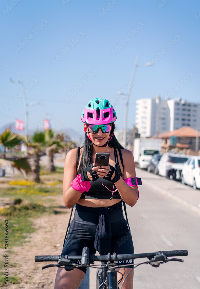 Naklejka premium female biker staring at cellphone and smiling on the bikeway in the city
