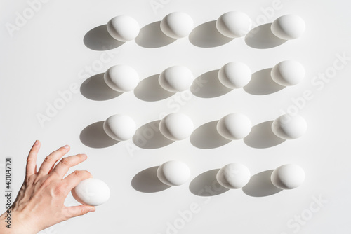 Easter white eggs pattern On A White Background. A hand is taking one away photo