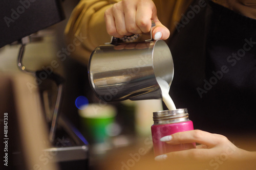 Young woman barista brews coffee and serves a customer in take away cafe.