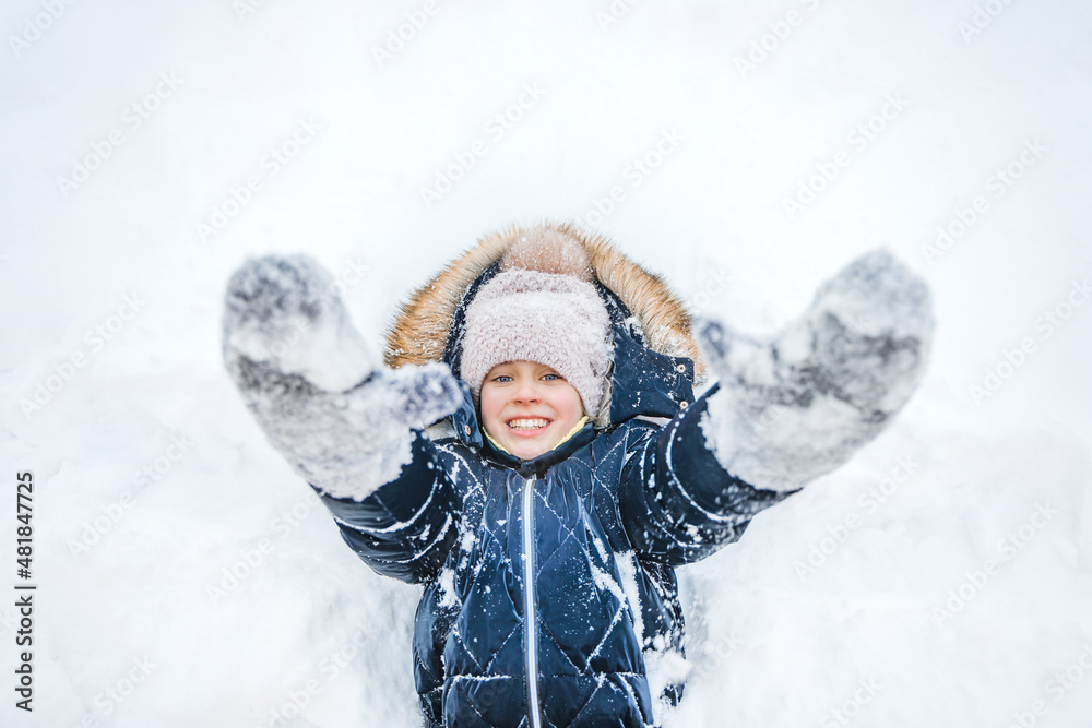 A happy smiling little girl lies in the snow with her arms outstretched to the camera in winter A happy smiling little girl lies in the snow with her arms outstretched to the camera in winter