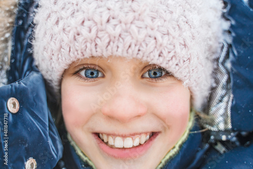Portrait of a happy smiling little girl in warm winter clothes in the snow in winter, close view