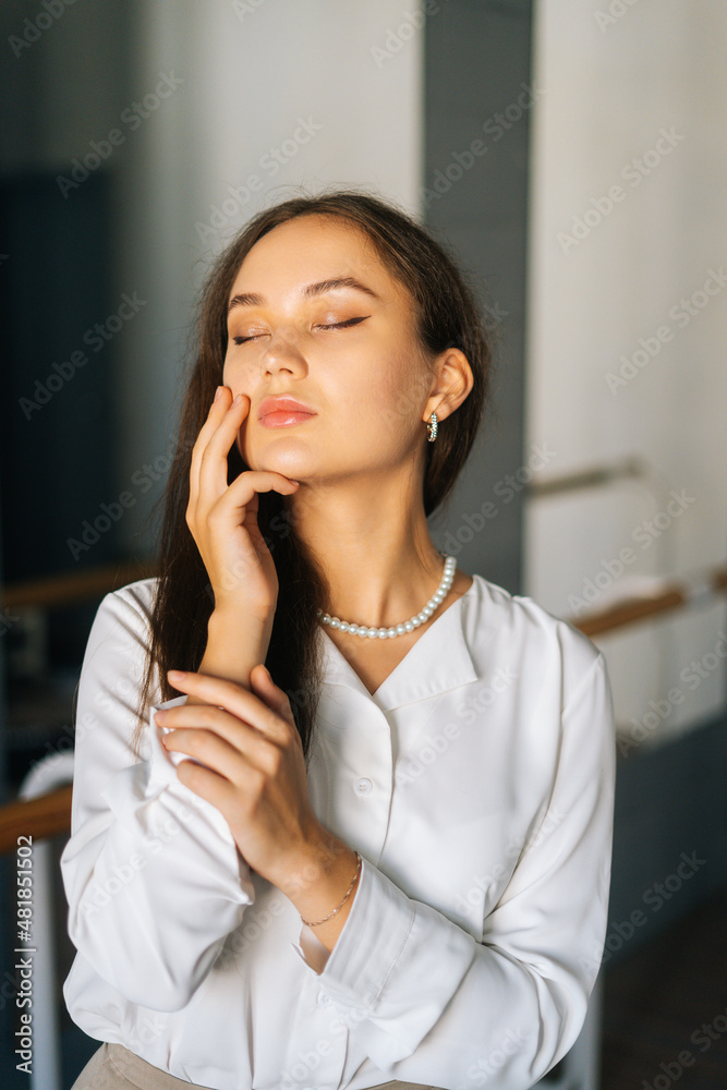 Close-up vertical portrait of confident young woman wearing stylish clothes standing in room with mirror, touching hair with hands, closed eyes Close-up vertical portrait of confident young woman wearing stylish clothes standing in room with mirror, touching hair with hands, closed eyes