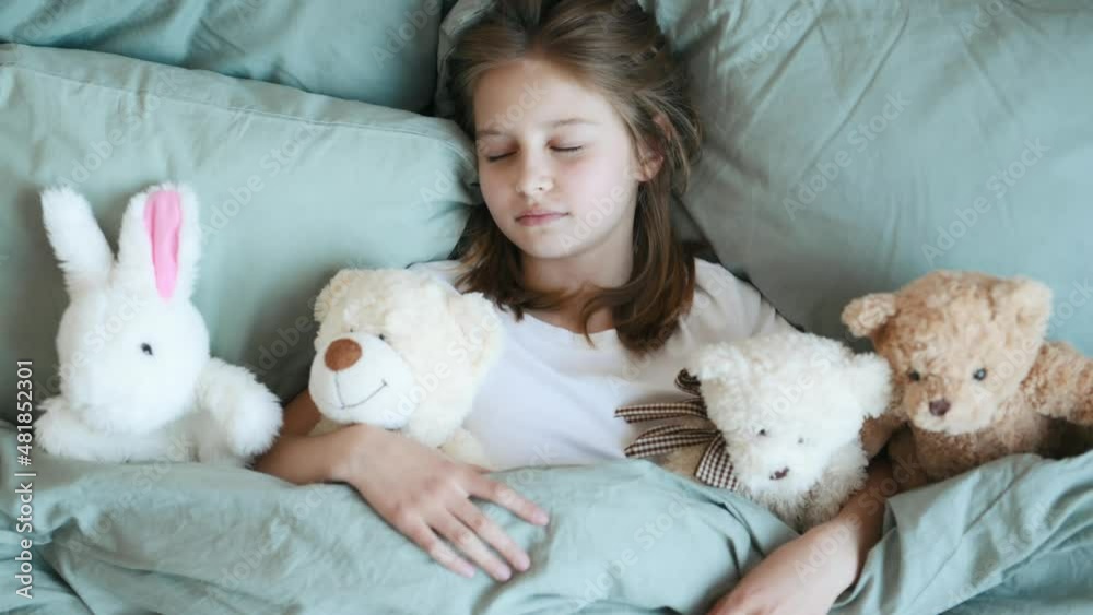 Cute girl sleeping with teddy bear and bunny toys lying in bed under blanket. Little child kid napping in bedroom Cute girl sleeping with teddy bear and bunny toys lying in bed under blanket. Little child kid napping in bedroom