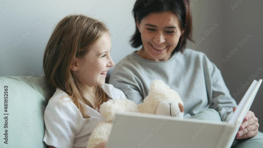 Mother and daughter reading book together in bed. Preteen girl with parent mom study at home, talking and smiling Mother and daughter reading book together in bed. Preteen girl with parent mom study at home, talking and smiling