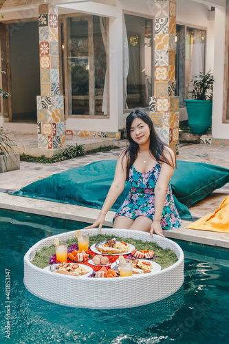 Pretty Asian woman eating breakfast in the pool, floating breakfast. © Karlie Studio