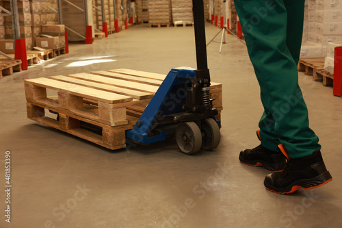 Worker moving wooden pallets with manual forklift in warehouse, closeup © New Africa