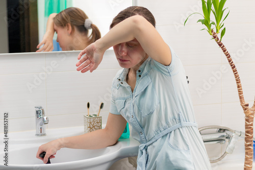 A young woman cleaner in a bright bathroom with a plunger to clear the blockage in her hands. On the wall is a mirror with a reflection. Green plant. Selective focus. Portrait